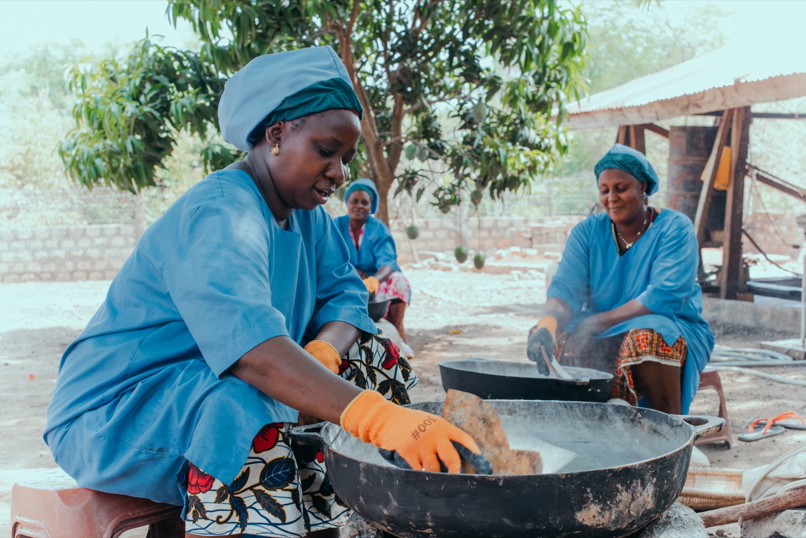 Des productrices torréfient le gari dans de grandes bassines, à l'unité de transformation de Faranah.